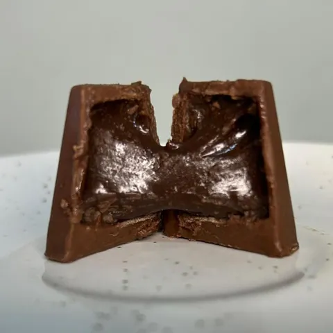 Bombom Cioccolato al Rum cortado ao meio, mostrando o recheio de creme de chocolate brilhante dentro da casca meio amarga