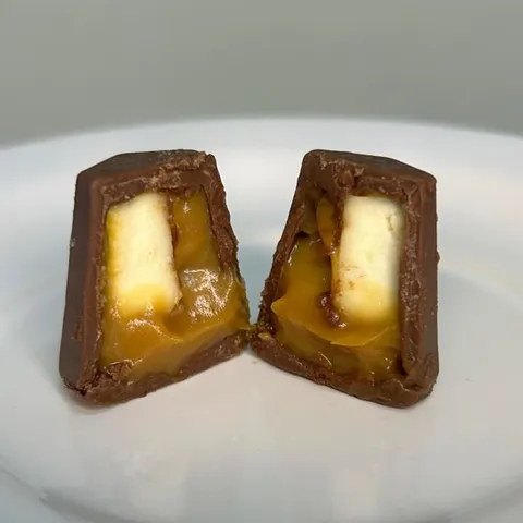Bombom Dolce Canastra cortado ao meio, mostrando o doce de leite caramelizado e o bloco de queijo canastra dentro da casca de chocolate