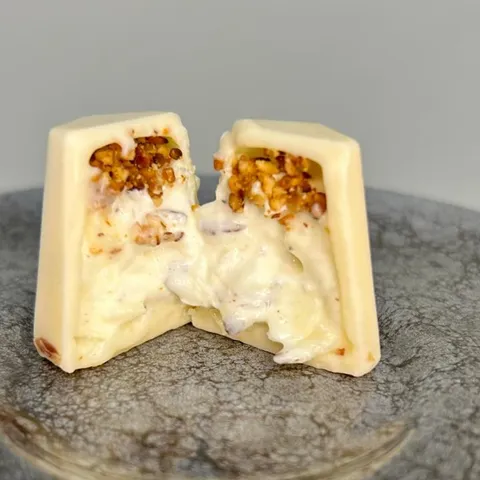 Bombom Nuvola Croccante cortado ao meio, mostrando a casca de chocolate branco e o recheio de creme aerado com coco e castanha de caju
