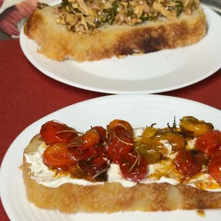 Fatia de focaccia coberta com coalhada seca e tomates confitados coloridos, servida em prato branco